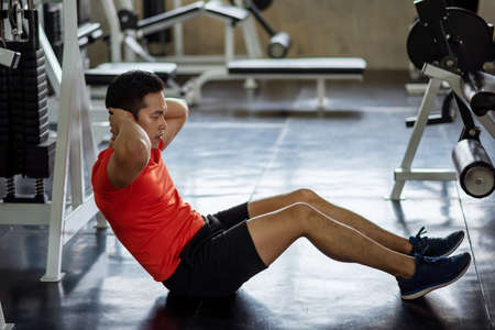 Asian Athlete young man sit ups and crunches exercising abdominal muscles to build six packs (upper and lower abs and the obliques) in fitness gym. Bodybuilding, sport, and healthy lifestyle concept.の写真素材