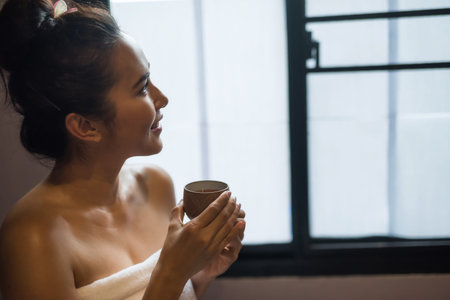 Smiling beautiful young Asian woman in white  hold cup of hot tea after having Thai massage in spa...