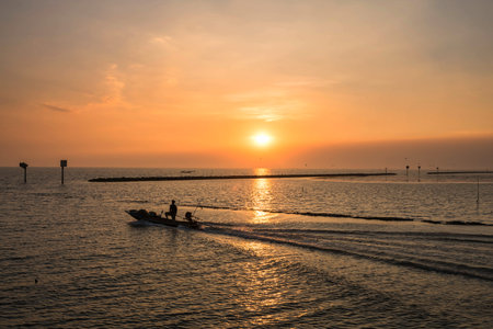 Silhouette fisherman sailing fishing boat from port at sunset of Bang Pu Sea, Samut Prakan,...