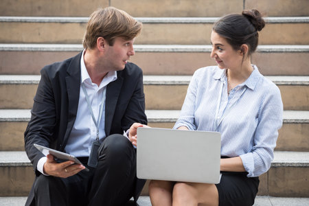 American businessman and businesswoman sit and discuss business plan in city by company laptop computer. teamwork meeting outside office.の写真素材