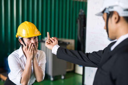 Aggressive factory manager show middle finger, fuck you, gesture sign to his stressed female worker for mistake in manufacturing warehouse. Bad behavior in working environment.の写真素材