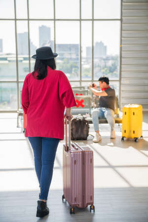 Female passanger walk and pull suitcase to sit at waiting area due to flight delay or wait for departure at airport terminal. She goes to see her friends at waiting area.の写真素材