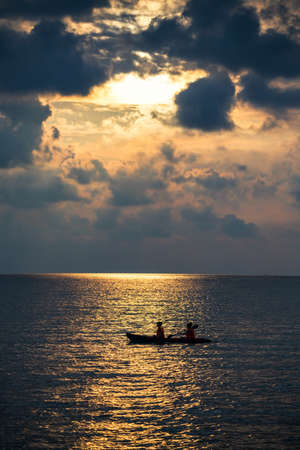 Silhouette two women kayaking boat on sea at sunset with light reflection on water and many cloud. Sport and recreation actvity during holiday vacation at summer in tropical country.の写真素材