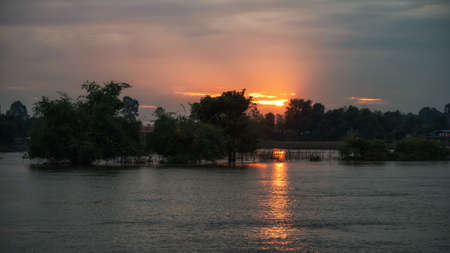 orange sunrise/sunset through cloudy sky with reflection on lake. sun shining over the the horizon and trees.の写真素材