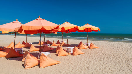 Orange beach umbrellas and bean bag chairs on white sand beach against blue sky in summer, Cha-am, Phetchaburi, Thailand. Holiday maker or vacation in tropical country,Siam.の写真素材