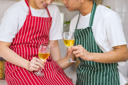 Closeup young  Asian  couple toast glasses of champagne to celebrate valentine's day. LGBT Asian men with apron sweet after cooking. Same sex family  in valentine's day.の写真素材