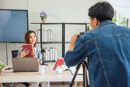 Behind the scene concept. Videographer discuss with young Asian female blogger to set up script before recording streaming live online with studio lighting. broadcasting vlogger. internet influencer.の写真素材