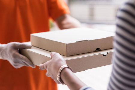 Pizza Delivery. Closeup hands of customer get food delivery from deliveryman in ornage uniform. New normal courrier food service by mobile application to prevent omicron pandemic.の写真素材