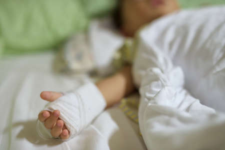 Closeup boy hand with saline intravenous, iv or drip, and bandage. He sleeps on a bed in hospital. Healthy insurance concept.の写真素材