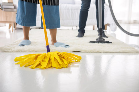 Closeup yellow mop and vacuum cleaner on carpet and floor in white bedroom. Couple routine house...