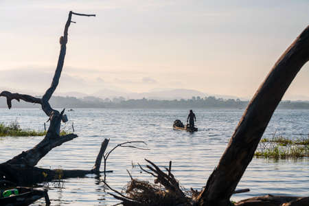 Silhouette fisherman on boat over bang phra reservoir with dead trees in morning, Sriracha, Chonburi, Thailand.の写真素材