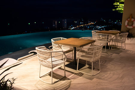Hotel rooftop pool at night with blur cityscape background. Relax seats by swimming pool.のeditorial素材