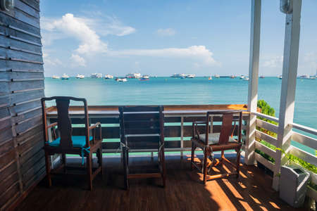 Wooden seats of coffee cafes by the sea in summer at Pattaya, Chonburi, Thailand. Homestay hostel or hotel by beach with many boats on ocean..の写真素材
