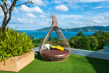 Rattan chair with soft seat on hotel roof top with beautiful view of Andaman sea and blue sky in Phuket, Thailand.の写真素材