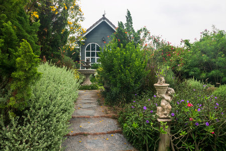 Footpath to fountain and modern wooden house in english cottage style. Beautiful garden design by many kinds of plants and flowers.の写真素材