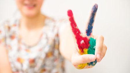 colorful paint hand with victory gesture of smiling Asian woman isolated on white background. Art...