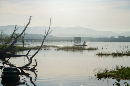 Fisherman on boat over bang phra reservoir catching fish by wooden stick, Siracha, Chonburi, Thailand. He pushing rot and then water splash.の写真素材