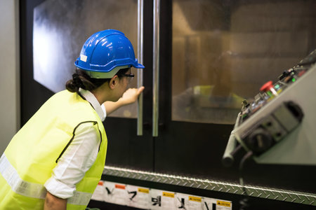 Waist up woman worker with hardhat and protection glasses check operation of cnc milling automate...