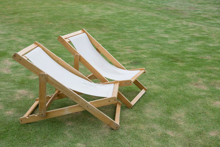 2 sunbed deck chairs on green grass in park for rest and relax.