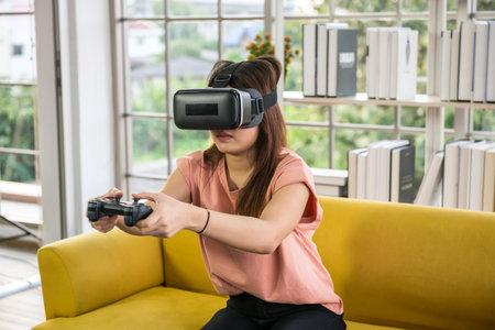 Serious asian woman playing video games with controller with virtual glasses in living room.の写真素材