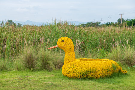 Big artificial yellow duckling or duck on green yard with long flower grass background at outdoor kid playground.の写真素材
