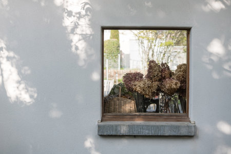Dry flower on basket decorated on window. View from outside with foliage light shade on white wallの写真素材
