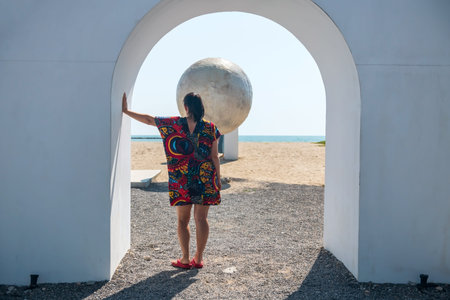 Rear of hipster woman with colorful dress standing on gate and look at artificial moon and sea...