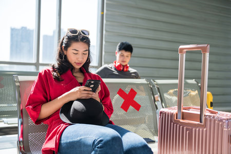 Bautiful asian young woman sit on waiting seats and play smartphone or mobie phone with light shade at airport departure terminal. She wait for boarding call.の写真素材