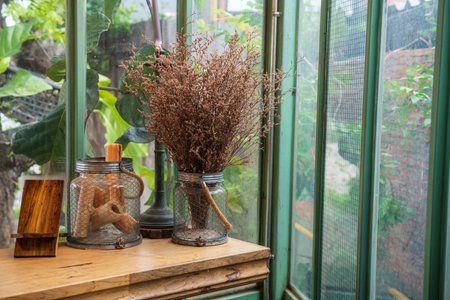 Bouquet of dry leaf in glass vase on wooden table by window at coffee cafe and restaurant. Interior...