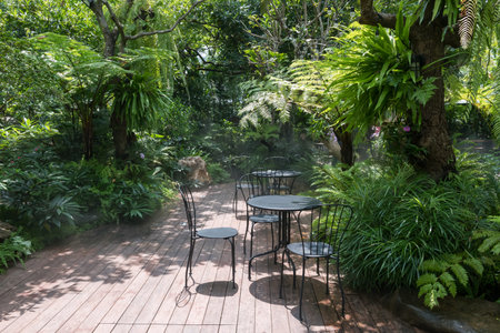 table and chairs on beautiful garden and artificial mist or fog in modern outdoor cafe and...