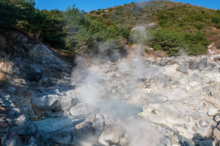 Jigoku hell valley at Mount Unzen onsen hot springs resort against blue sky, Nagasaki, Kyushu, Japan. Hot water, gases and steam spout out by geothermal heated volcanic spring field.の写真素材