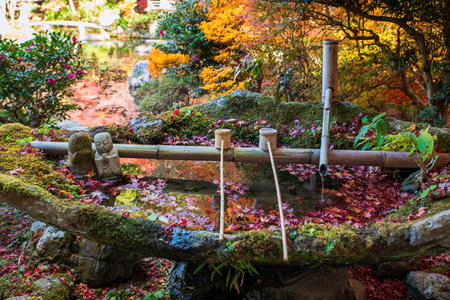 Bamboo fountain, hand washer wooden dipper, and Jizu Buddha statue on stone water basin of Bishamondo autumn garden, Kyoto, Japan. travel destination for tourist in Kansai on peak fall in December.の写真素材