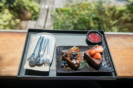 Homemade Chocolate cakes with fresh blueberry and strawberry sauce on wooden table by window in coffee shop cafe.の写真素材