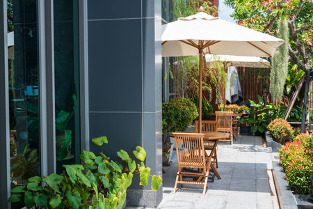 Outdoor wooden chairs and tables with parasols to relax at hotel balcony with plant decor in sunny day. Sitting place to drink hot coffee or take cigarettes.の写真素材