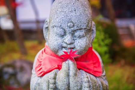 Red maple leaf on smiling Jizo Stone hand at autumn garden of Eikan-do or Eikando Zenrinji Temple,...