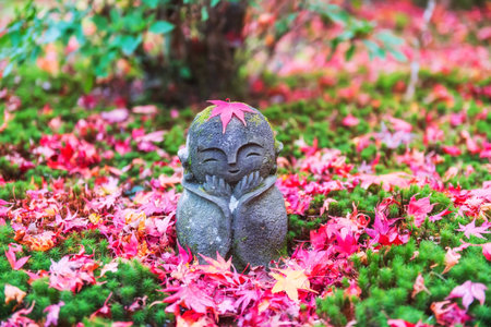 Jizo smiling Buddha statue with red autumn maple leaf on head at Enkoji temple garden, Kyoto, Japan. Famous travel destination of Rinzai Zen Buddhist sects in Kansai at fall momiji season..の写真素材