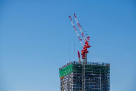tall building under construction with red crane against blue sky, Osaka, Japan.の写真素材