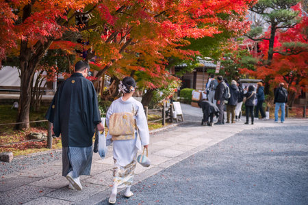 tourist couple in kimono and yukata enjoy colorful maple leaves in autumn at Eikando temple garden,...