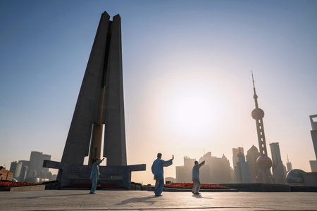 Chinese people exercise Tai Chi or Taiji at People's Heroes Memorial Tower of the Bund with pearl...