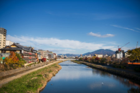 Blur city along Kamogawa River against autumn colors and blue sky on promenade next to Shijo Bridge...