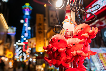 Octopus doll keychain souvenir at store in Shinsekai Osakas New World street by Tsutenkaku tower, Osaka, Japan. Travel destination with illuminated fancy billboard or signboard.の写真素材