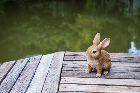 Rabbit door statue decor at wooden bridge by pond with tree reflection on water.の写真素材