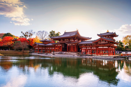 Phoenix Hall of Byodo-In temple with colorful autumn maple leaves and skyline reflection at sunset,...