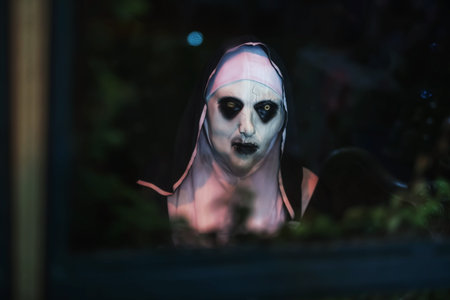 Spooky woman in devilish nun mask look through window and strangle hand gesture at night. 2025...