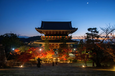 People on steps view red maple tree light up by Kurodani Konkai Komyoji temple mountain Sanmon gate at dusk with moon in autumn, Kyoto, Japan. travel destination for sightseeing Kansai fall illusion.の写真素材