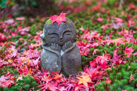 Smiling Jizo Buddha stone statue with red maple leaf and orange heart on head at Enko-ji temple...