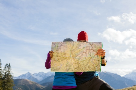 Man and woman hikers hiking in mountains. Young couple looking at map and planning trip or get lost. Selective focus on a mapの写真素材