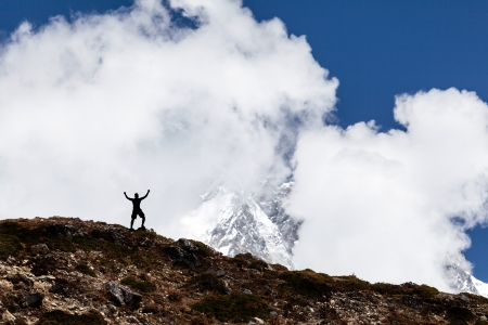 Man hiking silhouette in mountains, sunset and clouds. Male climber hiker arms outstretched on top of mountain after success climbing looking at beautiful landscape.の写真素材