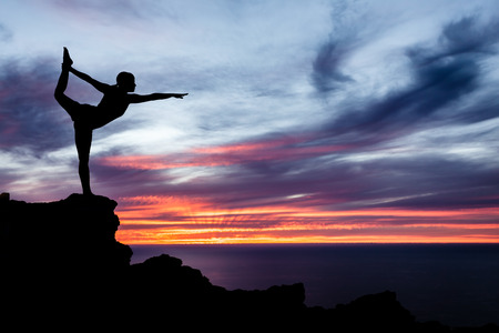 Young woman doing yoga, sunset silhouette in mountains over ocean and skyの写真素材