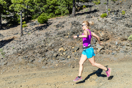 Young woman trail running in mountains on sunny summer day. Beauty female runner jogging and exercising outdoors in nature, rocky trail footpath on La Palma, Canary Islandsの写真素材